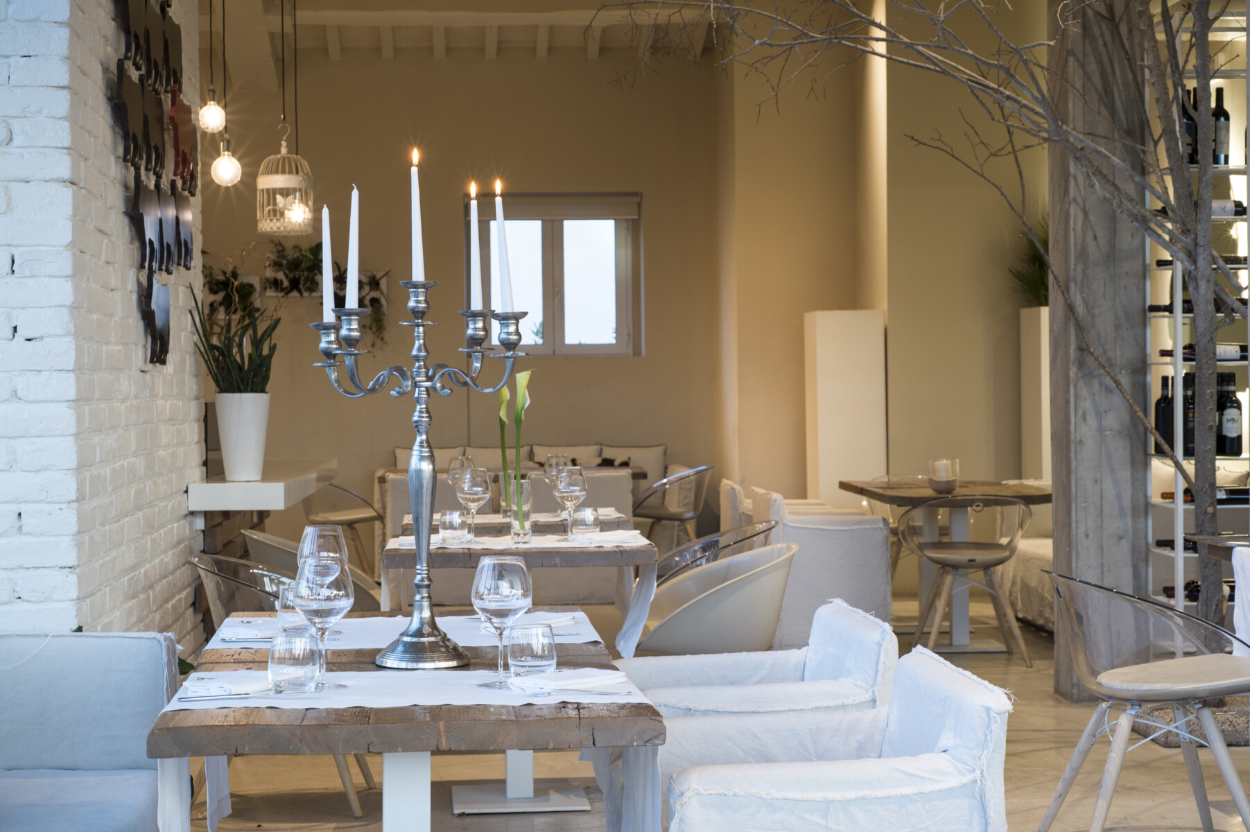 Sala ristorante con tavoli apparecchiati, candelabro acceso al centro e parete in mattoni con decorazioni a silhouette