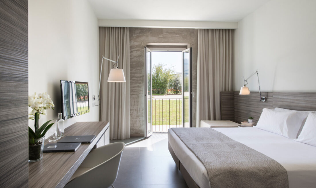 Camera Garden con letto bianco, testata in legno, corridoio con armadio e lampade di design a braccio sulle pareti