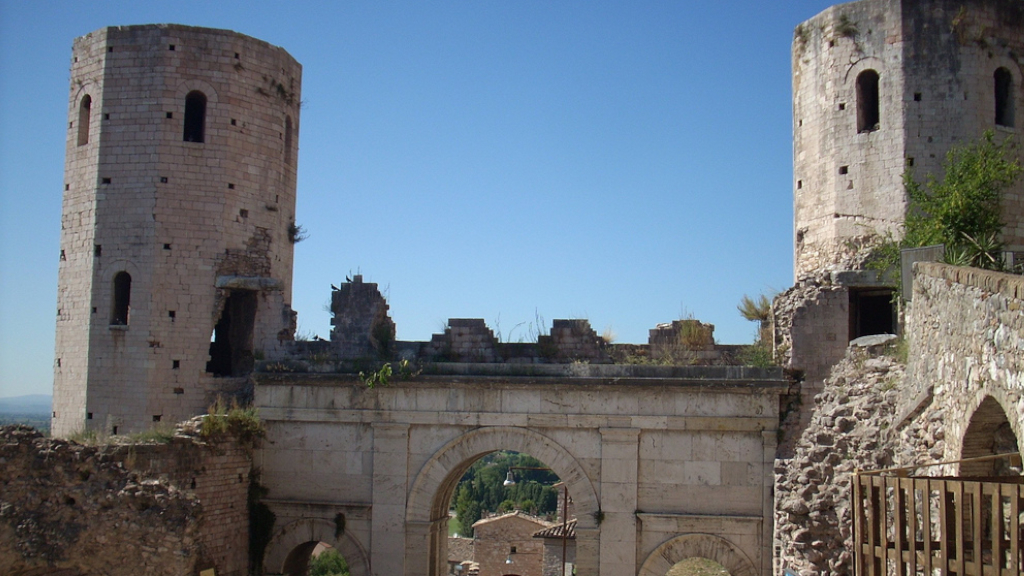 Porta Venere a Spello con torri medievali in pietra calcarea, vegetazione sulle sommit├á e tetti in cotto del borgo visibili dal varco centrale