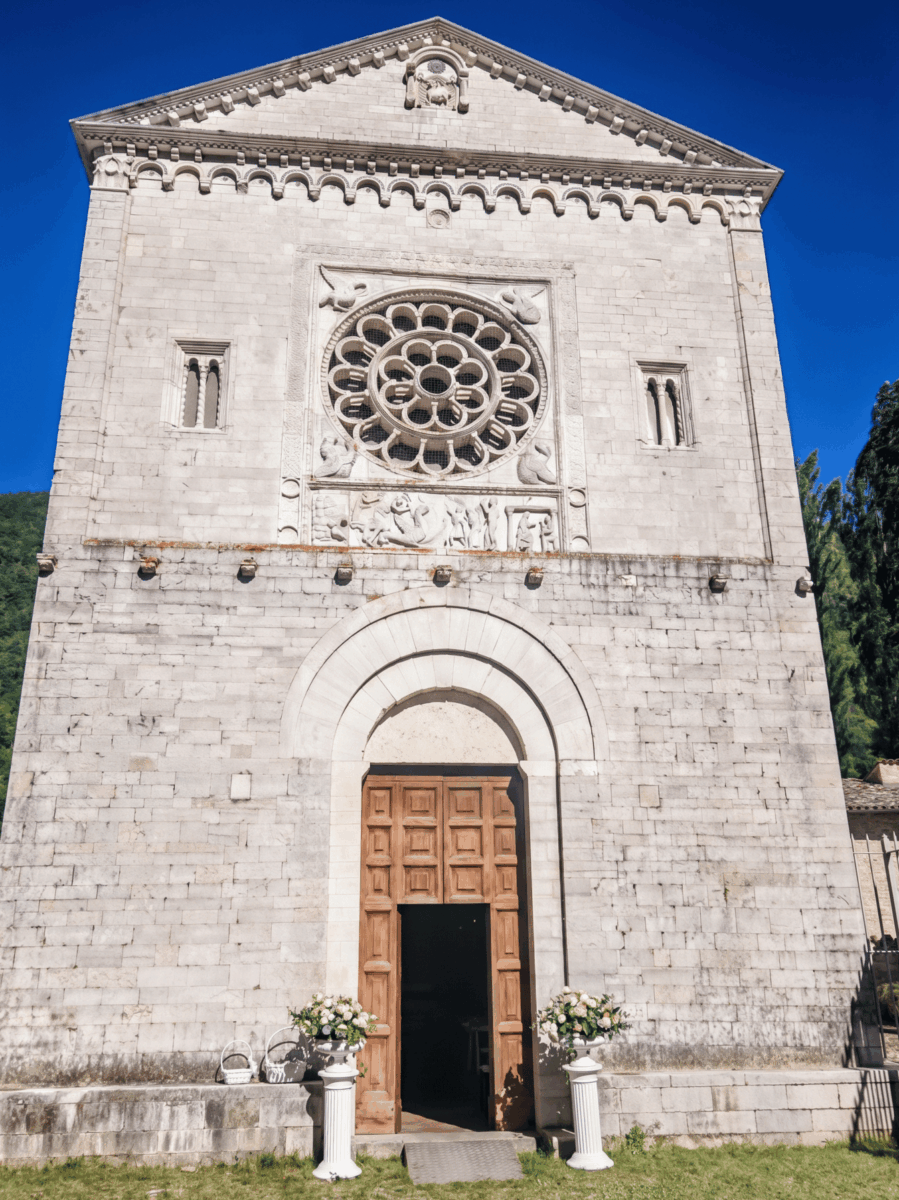 Facciata in pietra calcarea dell'Abbazia dei Santi Felice e Mauro a Castel San Felice, con portale d'ingresso, rosone istoriato e bassorilievo romanico